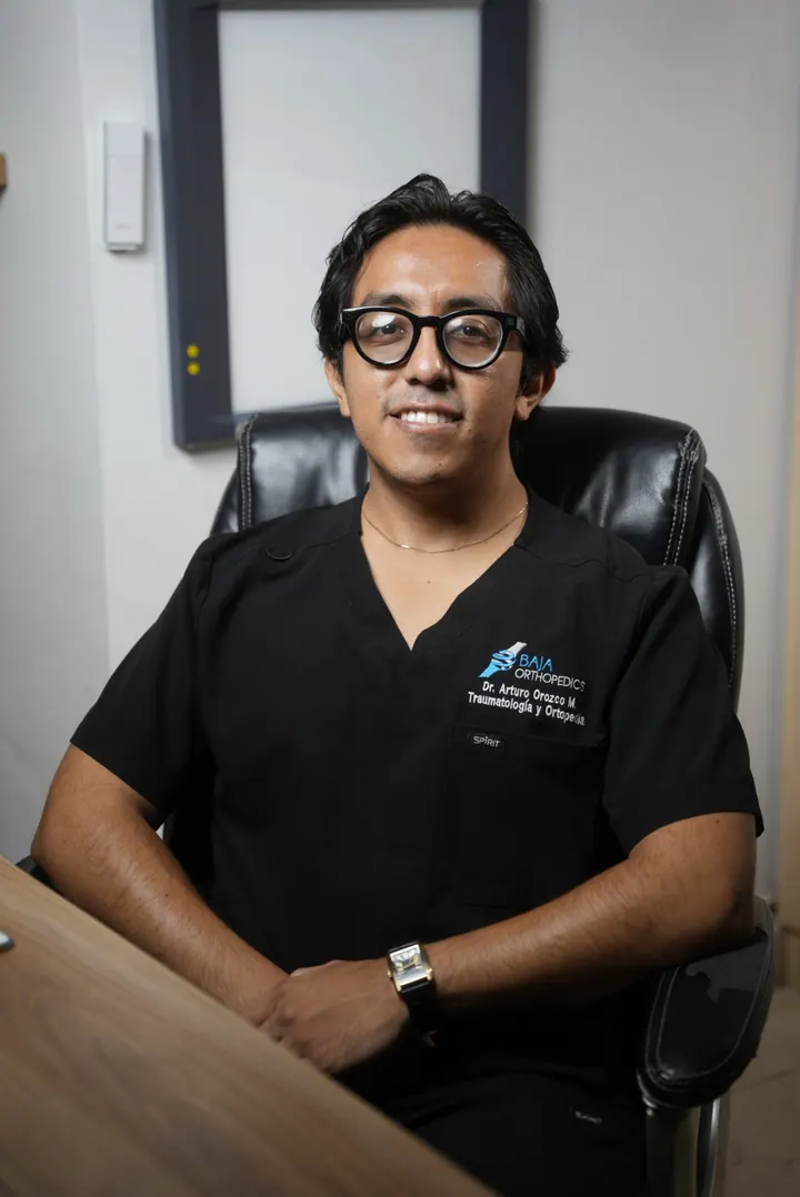 El Dr. Arturo Orozco sentado a su escritorio, en uniforme quirúrgico negro